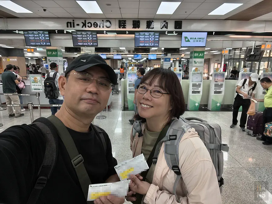 翰斯與 Kay 在台北松山機場立榮航空櫃檯前,拿著登機證自拍