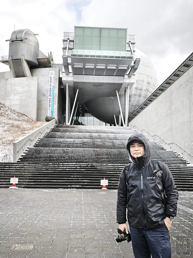 翰斯在下著雪的佐賀縣立宇宙科學館前方階梯留影