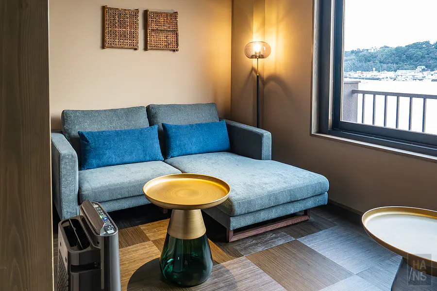客房內放鬆的灰藍色布質沙發區與充滿現代感的金屬圓型邊桌