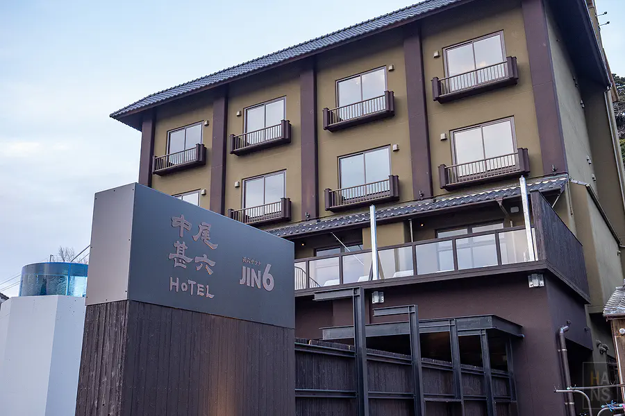 傍晚時分的中尾甚六HOTEL本館外觀與入口處精心佈置的松樹盆景及暖色照明