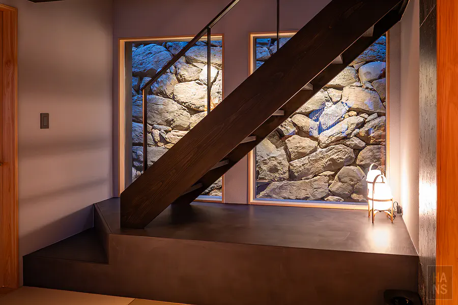 浦田別邸一樓通往二樓的現代黑色鐵件樓梯與充滿歷史感的粗獷石牆設計
