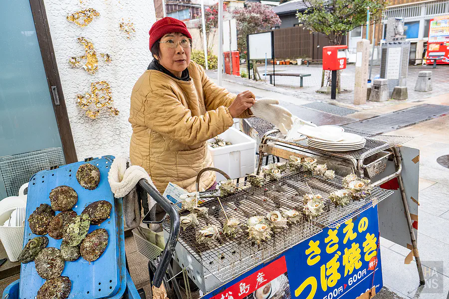 親切的攤販阿姨正在烤網上精心製作現烤蠑螺