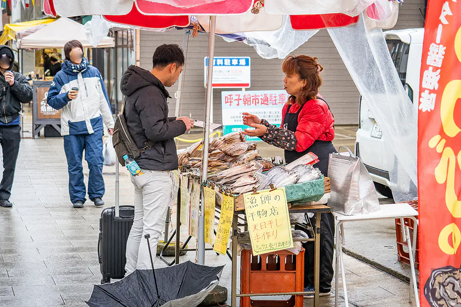 雨中在呼子朝市向攤販阿姨採買海鮮乾貨的遊客