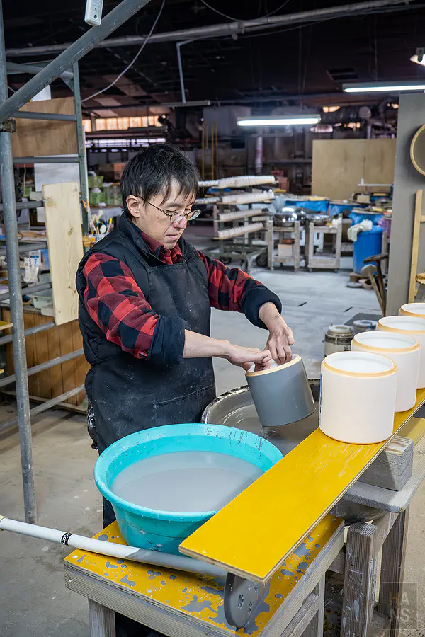 職人專注地為圓筒狀瓷器進行均勻的施釉作業