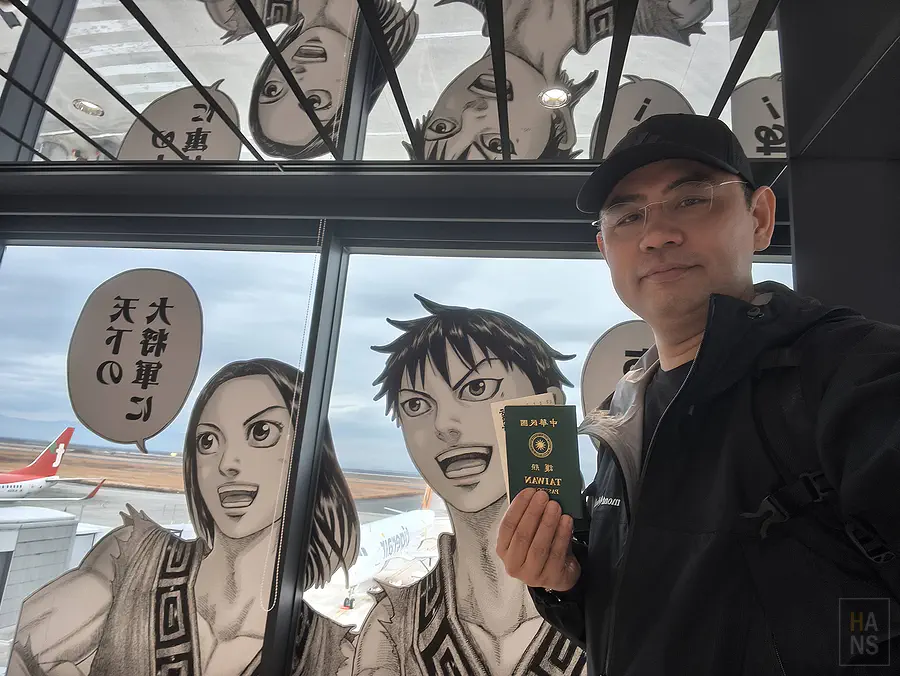 翰斯在機場展望台拿著護照與王者天下角色窗貼自拍合照