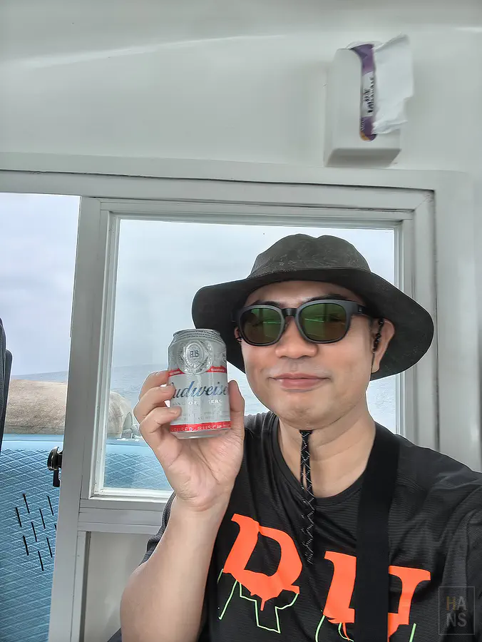 翰斯在遊艇船舷邊迎著海風暢飲免費提供的冰涼罐裝啤酒