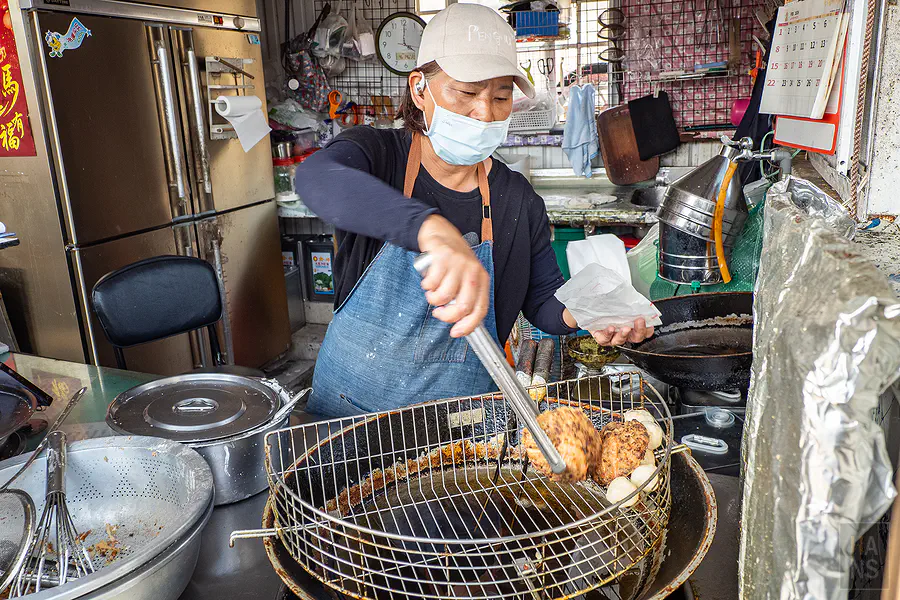 老闆娘熟練地將豐富內餡鋪滿勺子，準備下鍋油炸的誘人畫面